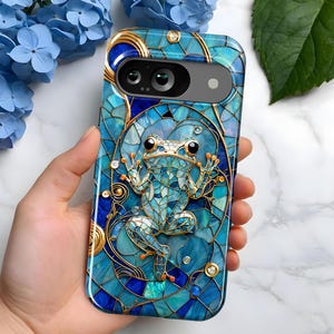 Puede incluir: Una funda para teléfono azul y dorada con un diseño de mosaico que presenta una rana. La funda tiene un recorte para el objetivo de la cámara.