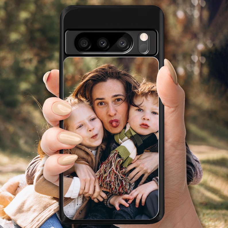 May include: A black phone case with a photo of three people. The photo shows a woman with her tongue sticking out, and two children, one on each side of her. The woman is wearing a scarf with a striped pattern.