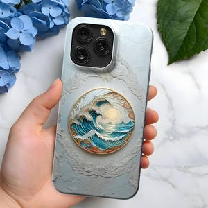 May include: A white phone case with a raised, textured design. The case features a round, blue and gold sticker with a wave design. The sticker has a white background and a sun in the top right corner.