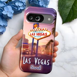 May include: A phone case featuring a Las Vegas sign design with the text "Welcome to Fabulous Las Vegas Nevada." The case has a sunset background with palm trees and the name "Sarah" below the city name.