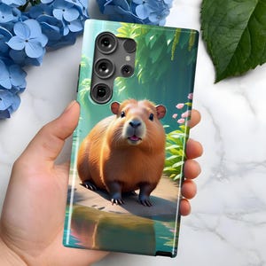 May include: A phone case with a green and brown jungle scene featuring a capybara. The case has a black camera bump with three lenses.