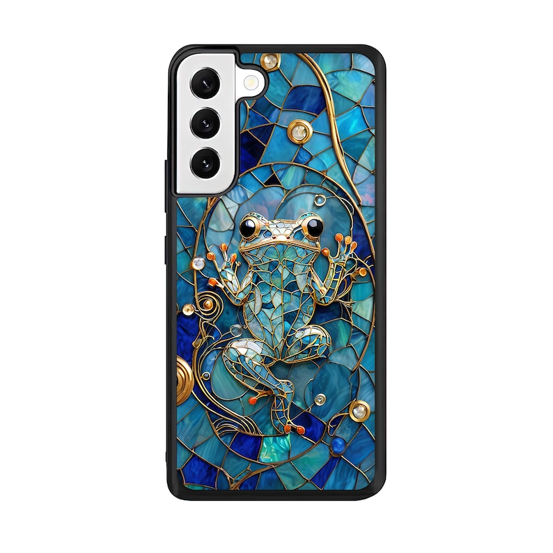 Peut inclure: Une coque de t&eacute;l&eacute;phone bleue et dor&eacute;e avec un motif en mosa&iuml;que repr&eacute;sentant une grenouille. La coque a une d&eacute;coupe pour l'objectif de l'appareil photo.