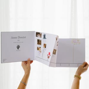May include: A white educational timeline book titled Anno Domini AD In the Year of Our Lord, featuring a tree logo, historical illustrations, and handwritten notes including The First Great Awakening, displayed in an open, multi-panel format.