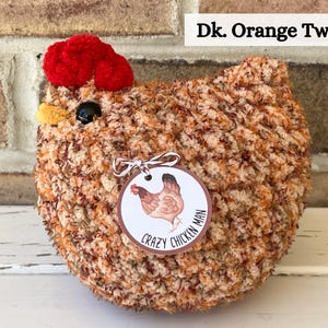 Puede incluir: Un juguete de peluche de pollo tejido a crochet con una cresta roja y un cuerpo de tweed marr&oacute;n y naranja. El juguete tiene una etiqueta que dice "Crazy Chicken Man".