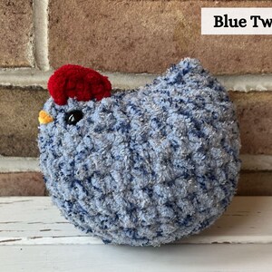 Puede incluir: Un pollo de crochet azul y plateado con una cresta de fieltro rojo. El pollo est&aacute; sentado sobre una superficie blanca. Blue Tweed.