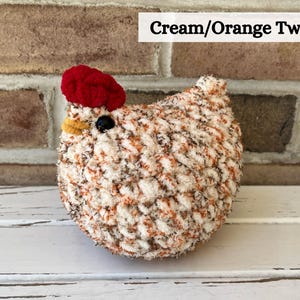 Puede incluir: Pollo de crochet de tweed crema y naranja con cresta roja y pico amarillo.