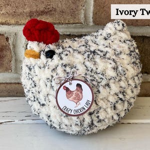 Puede incluir: Un pollo de crochet blanco y negro con un sombrero de crochet rojo. El pollo tiene una etiqueta que dice "Crazy Chicken Lady".
