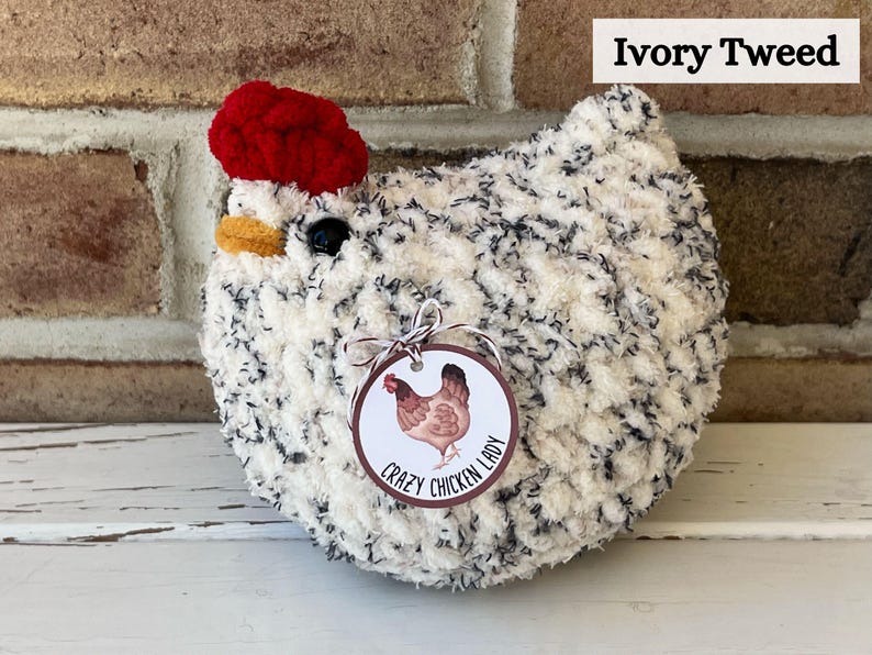 Puede incluir: Un pollo de crochet blanco y negro con un sombrero de crochet rojo. El pollo tiene una etiqueta que dice "Crazy Chicken Lady".