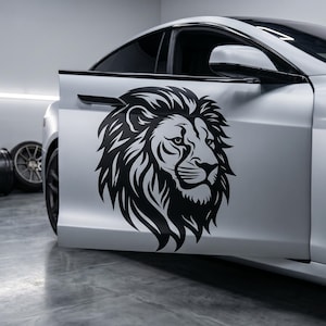 以下が含まれることがあります： マットホワイトの車のドアに、ライオンの頭部を横顔で描いた大きな黒いビニールデカールが貼られています。ライオンのグラフィックは、流れるようなたてがみのディテールとシャープな顔立ちが特徴で、車両のドアの滑らかな表面に直接貼り付けられています。