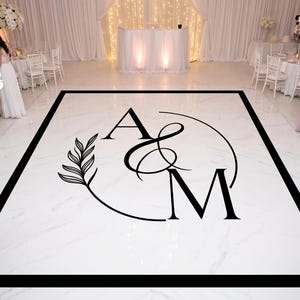 May include: A rectangular white dance floor with a marble pattern and a thick black border. In the center, a black graphic features the letters A and M, an ampersand, a circular line, and a leafy branch design printed on the floor surface.