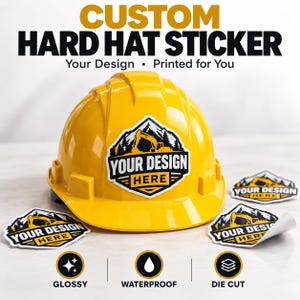 May include: A bright yellow hard hat featuring a custom sticker with a black and white mountain and excavator graphic and the text YOUR DESIGN HERE. Three additional matching stickers are displayed, with one partially peeled back.