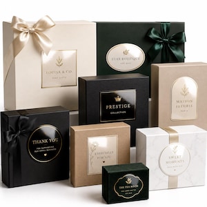 May include: A collection of square and rectangular gift boxes in various colors including cream, dark green, black, and tan, featuring satin ribbons and gold-foiled labels with brand names like Louisa & Co., Prestige, and Maison Fleurie.
