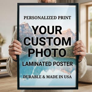 May include: A rectangular laminated poster in a thin black frame featuring a landscape photograph of mountains reflected in a lake. The text reads: PERSONALIZED PRINT, YOUR CUSTOM PHOTO, LAMINATED POSTER, DURABLE & MADE IN USA.