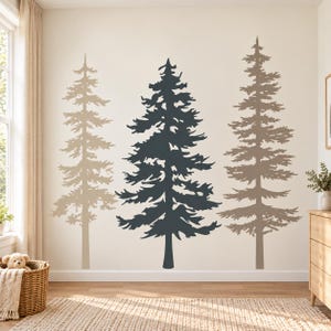 Può includere: Un set di adesivi murali con tre pini in fila. I due alberi esterni sono marrone chiaro, mentre l'albero centrale è grigio antracite scuro. Ogni albero presenta una silhouette dettagliata con rami che partono dal tronco.
