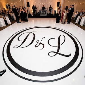 Puede incluir: Un gran adhesivo circular blanco para pista de baile con un borde negro grueso y las letras monograma D & L estilizadas en negro en el centro. El diseño está impreso sobre una superficie lisa, creando un punto focal para un evento formal.
