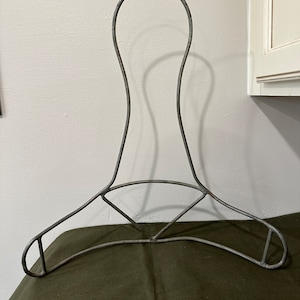 May include: A vintage metal hanger with a unique curved design. The hanger is made of wire and has a silver finish.
