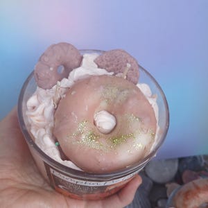 Op de afbeelding: Een glazen pot met een roze geglazuurde donut, witte slagroom en bruine en roze sprinkles. De kaars is gelabeld "Pumpkin Spice"