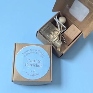 May include: A car air freshener set in a small cardboard box. The box contains a glass bottle, wooden sticks, and a wooden block. The label reads "Pearl & Petrichor" and "8 ml Car Diffuser". The product is from Bubble Bunny Bath Co.