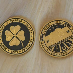 May include: Two gold-coloured coins with black centres. One coin features a four-leaf clover with the words "FORTUNE", "SUCCESS", "HEALTH", "HAPPINESS", "LOVE", and "PEACE" around the edge. The other coin features an elephant with the words "GOOD LUCK", "177", "FORTUNA IN ATERNUM", "ACCOMPANY THE BEARER" around the edge.
