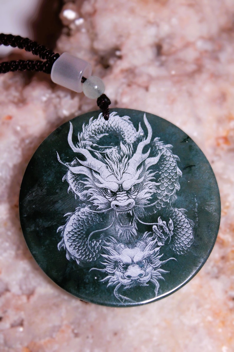 May include: Dark green circular pendant featuring a detailed white dragon design. The dragon is intricately carved, showcasing scales, claws, and a fierce expression. The pendant hangs from a black cord with a white clasp.