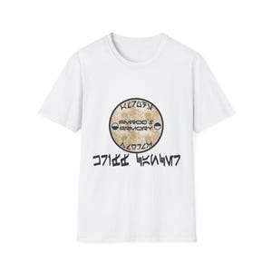 May include: A white short-sleeved t-shirt featuring a central circular graphic with a mottled tan texture. The graphic displays the text AMROD'S ARMORY in black, flanked by two small half-circle icons, with stylized characters above and below.