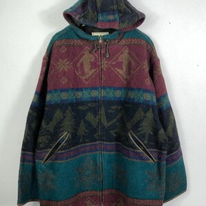 Op de afbeelding: Een jas met capuchon met een kleurrijk geometrisch patroon. De jas heeft een volledige ritssluiting, twee voorzakken en een capuchon. De kleuren zijn bordeauxrood, teal, marineblauw en bruin. De jas heeft een vintage, outdoor uitstraling.