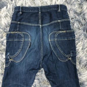 Op de afbeelding: Donkerblauwe denim jeans met unieke zakdetails. De jeans hebben gebogen zakken op de achterkant met decoratieve stiksels en een klassiek vijf-zakken ontwerp. De denim heeft een licht vervaagde uitstraling.