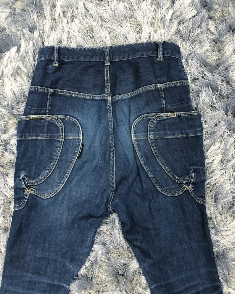 Op de afbeelding: Donkerblauwe denim jeans met unieke zakdetails. De jeans hebben gebogen zakken op de achterkant met decoratieve stiksels en een klassiek vijf-zakken ontwerp. De denim heeft een licht vervaagde uitstraling.