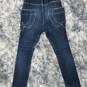 Op de afbeelding: Donkerblauwe denim jeans met unieke zakdetails. De jeans heeft grote, gebogen zakken op de achterkant en een hoge taille. De denim heeft subtiele vervaging en slijtage, wat het een vintage look geeft. De jeans ligt plat op een getextureerd oppervlak.