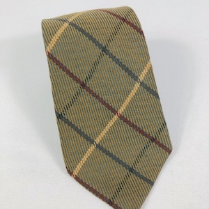 以下が含まれることがあります： 薄茶色のチェック柄ネクタイ。細い赤、青、黄色のラインが繰り返されるパターンです。ネクタイは質感のある生地で作られており、白い背景に表示されています。クラシックなアクセサリーです。