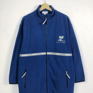 May include: A blue fleece jacket with a full-length zipper, featuring a high collar and two zippered pockets. The jacket has a white band across the chest with the brand name. The brand logo is on the chest. Black trim accents the cuffs and hem.