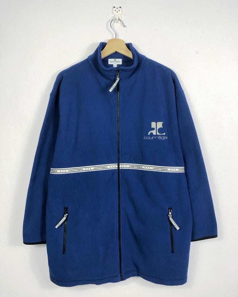 May include: A blue fleece jacket with a full-length zipper, featuring a high collar and two zippered pockets. The jacket has a white band across the chest with the brand name. The brand logo is on the chest. Black trim accents the cuffs and hem.