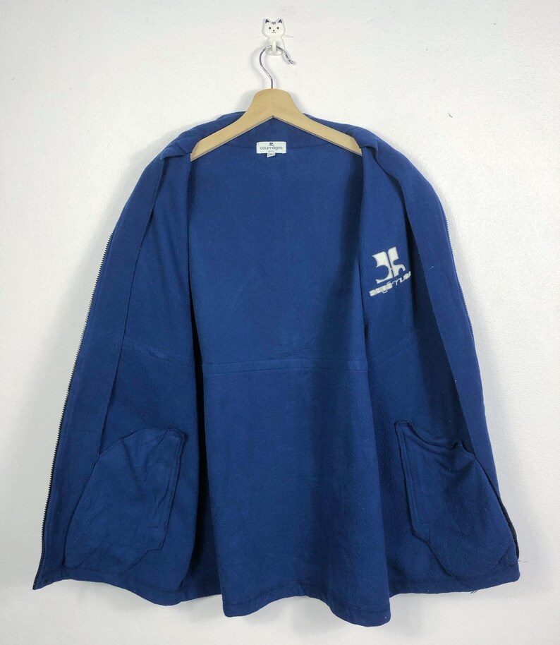 May include: A navy blue jacket with a full zipper and two front pockets. The jacket is hanging on a wooden hanger. The inside of the jacket has a white logo and the text "SPORTLINE" printed on the upper right side.