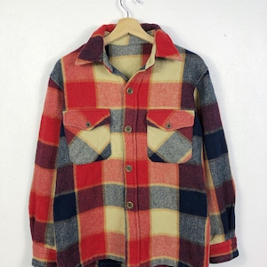 以下が含まれることがあります： クラシックなチェック柄のヴィンテージボタンダウンフランネルシャツ。赤、ネイビー、ベージュ、バーガンディの色使いです。胸ポケットが2つ、襟が付いています。木製のハンガーにかかっています。