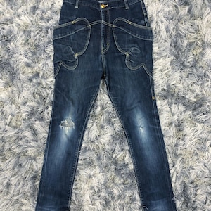 Op de afbeelding: Donkerblauwe denim jeans met unieke zakdetails en een beschadigde knie. De jeans heeft een hoge taille en een knoopsluiting. De denim is van gemiddeld gewicht en de jeans heeft een slanke pasvorm.
