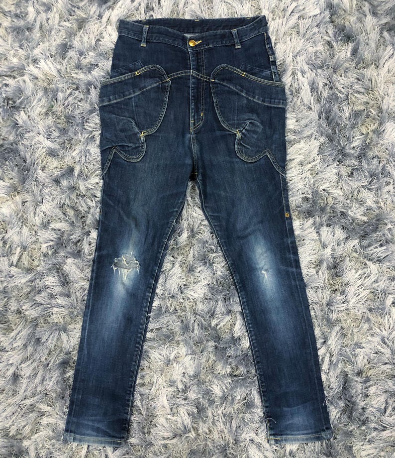Op de afbeelding: Donkerblauwe denim jeans met unieke zakdetails en een beschadigde knie. De jeans heeft een hoge taille en een knoopsluiting. De denim is van gemiddeld gewicht en de jeans heeft een slanke pasvorm.