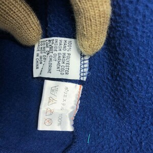 May include: Close-up of a blue fabric with attached care labels. The labels provide washing instructions, including hand wash cold, do not bleach, and do not iron. The fabric is made of 100% polyester and made in China.