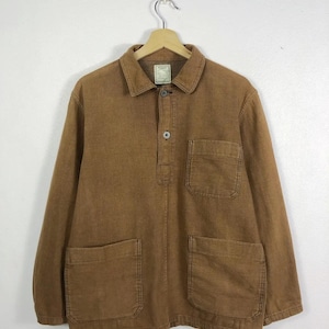 May include: A brown long-sleeved jacket with a collar and two large front pockets. The jacket has a button-down closure and two additional chest pockets. The garment is hanging on a wooden hanger.