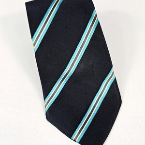 Könnte beinhalten: Marineblaue Krawatte mit diagonalen Streifen in Hellblau, Grau und Weiß. Die Krawatte ist aus glattem Stoff gefertigt und eignet sich für formelle oder geschäftliche Anlässe. Ein klassisches Accessoire.