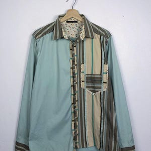 May include: A long-sleeved button-down shirt with a patchwork design. The shirt is made of a light blue fabric with a striped pattern on the right side. The shirt has a floral print lining.