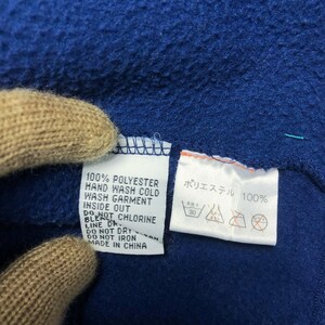 May include: Close-up of a blue fleece fabric with two white tags. One tag reads "100% POLYESTER" and care instructions. The other tag has Japanese text and washing symbols. The fabric is made in China.
