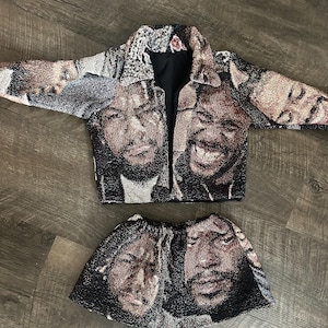 May include: A two-piece tapestry set featuring a jacket and a skirt. The jacket has a collared neckline and long sleeves. The set is made of a woven fabric with a repeating pattern of faces in shades of brown, black, and beige.