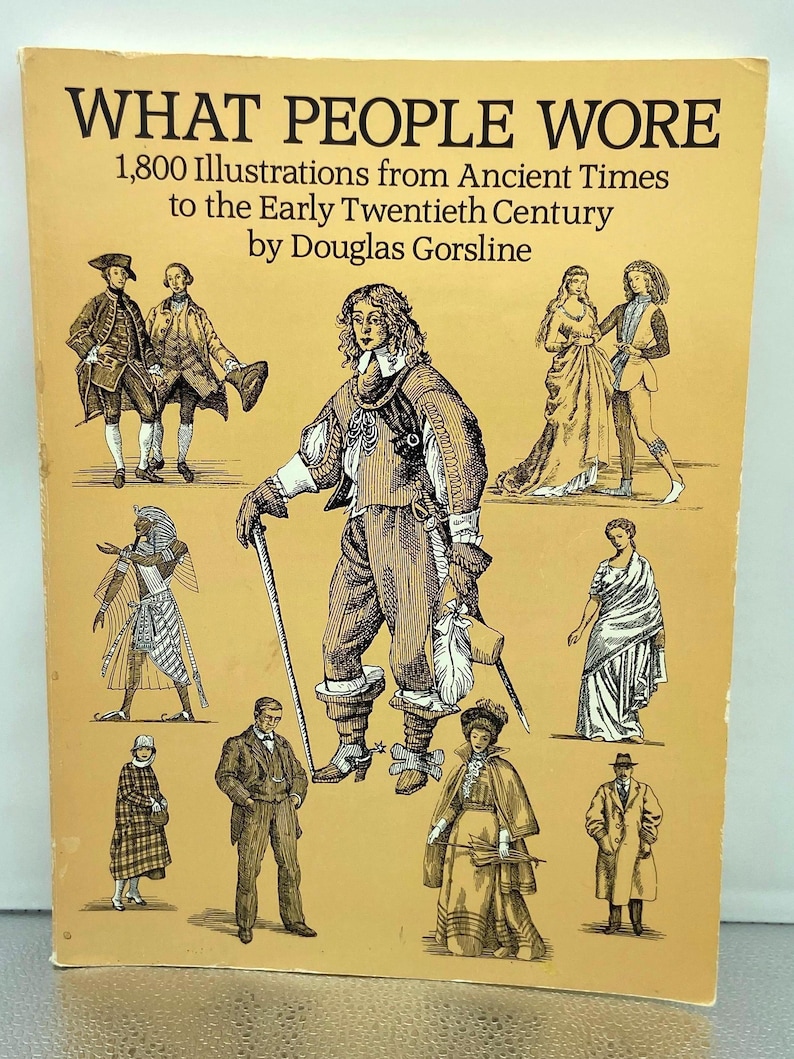 May include: A vintage book cover titled "WHAT PEOPLE WORE" with illustrations from ancient times to the early twentieth century. The cover features drawings of people in historical clothing, in shades of brown and tan.