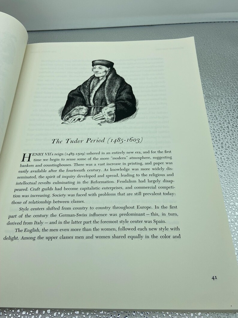 May include: An illustration of a person from The Tudor Period (1485-1603) on a book page. The image is a black and white drawing of a person wearing a hat and a fur-lined coat. The text below the image reads "The Tudor Period (1485-1603)".