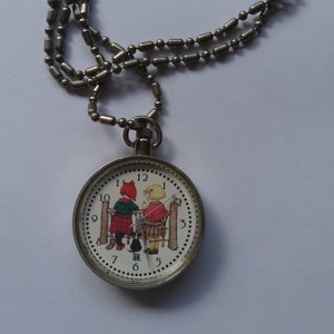 May include: A silver chain necklace with a round pocket watch pendant. The watch face features a white background with black numbers and a colorful illustration of two children standing by a fence.