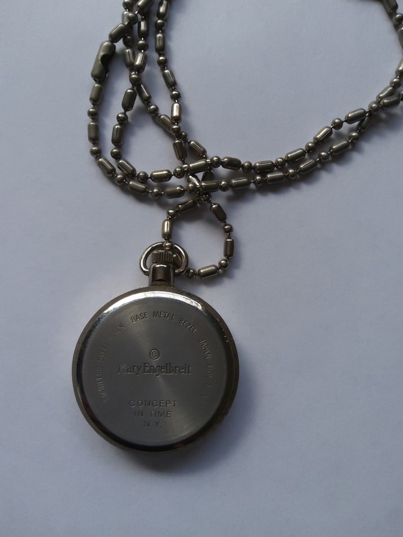 May include: Silver pocket watch with a chain. The back of the watch has the text "Mary Engelbreit" and "Concept in Time NY".