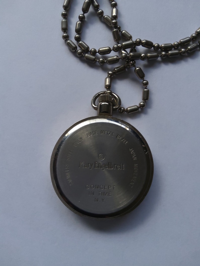 May include: Silver pocket watch with a chain. The back of the watch has the text "Mary Engelbreit" and "Concept in Time NY".