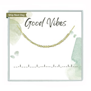 May include: A gold necklace with a delicate chain and small beads. The necklace is displayed in a white box with the words "Good Vibes" written in black cursive.