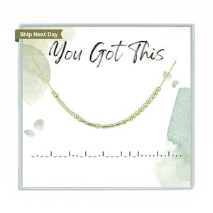 May include: A gold and silver beaded necklace with the words "You Got This" on a white background with green watercolour accents.