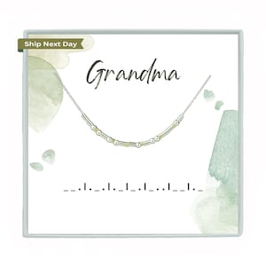 May include: A silver necklace with gold beads and the word "Grandma" written in cursive on a white background with green watercolor accents.